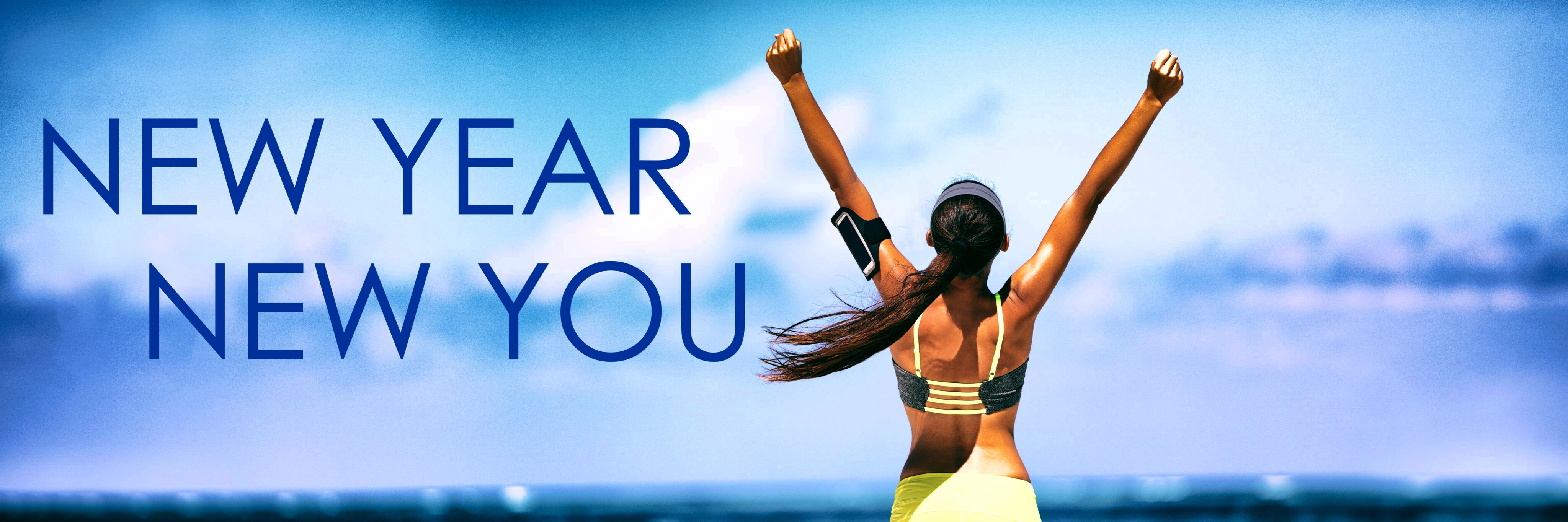 Woman with arms raised facing the sea under a sky with "new year new you" text overlay.