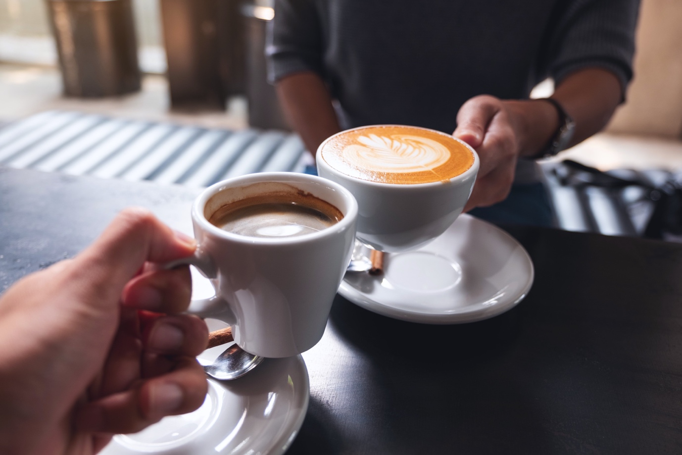 Two people holding cups of coffee, one cup showcasing latte art, in a casual setting.