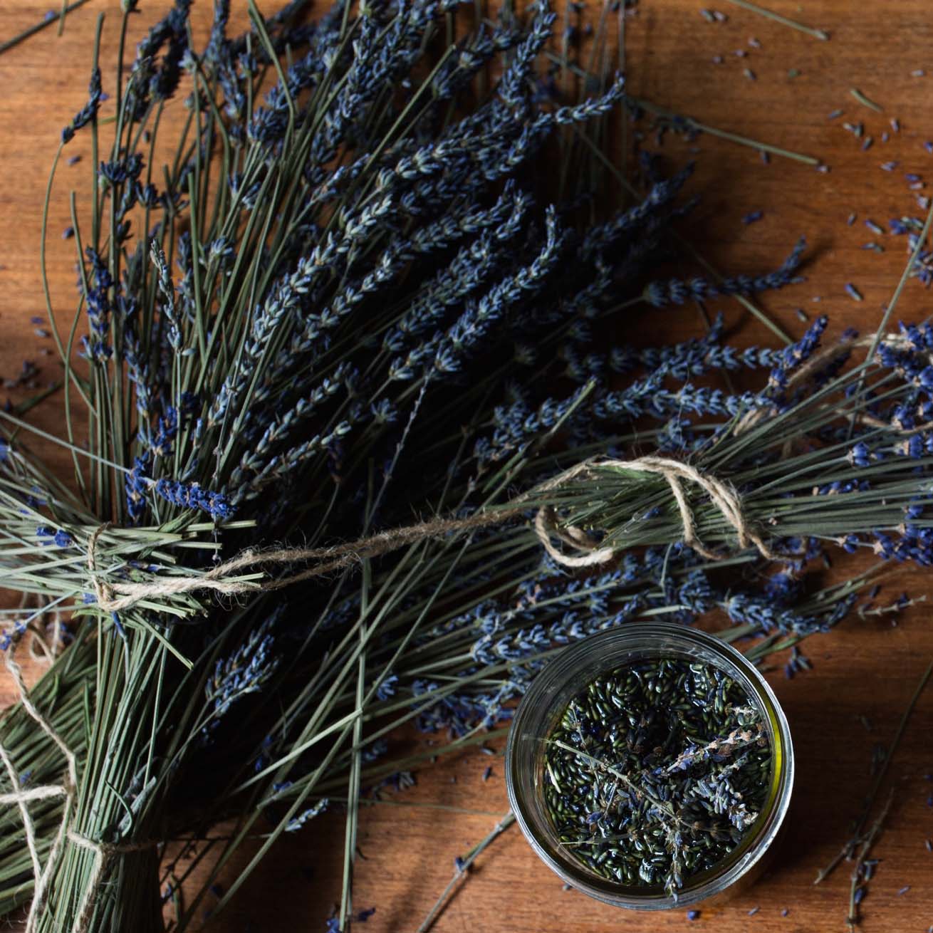 Dried lavender bundles and a glass jar containing lavender buds on a wooden surface.