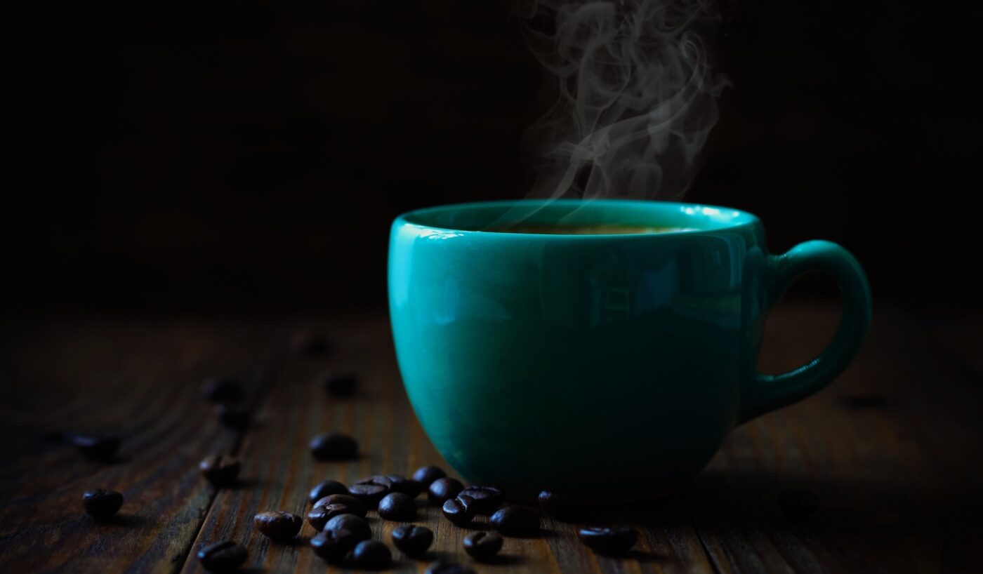 A teal coffee cup with steam rising from it, surrounded by scattered coffee beans on a dark wooden surface.