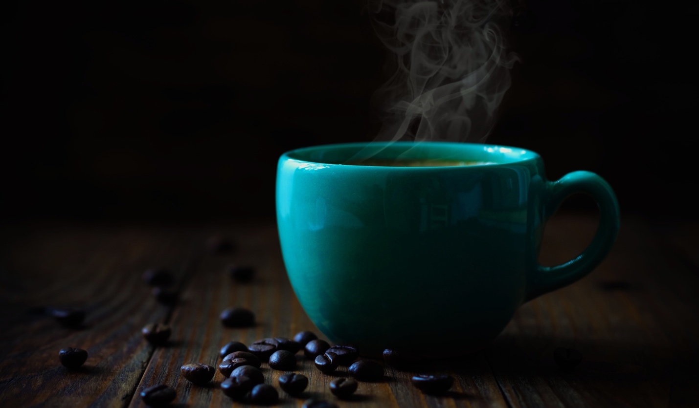 A teal coffee cup with steam rising from it, surrounded by scattered coffee beans on a dark wooden surface.