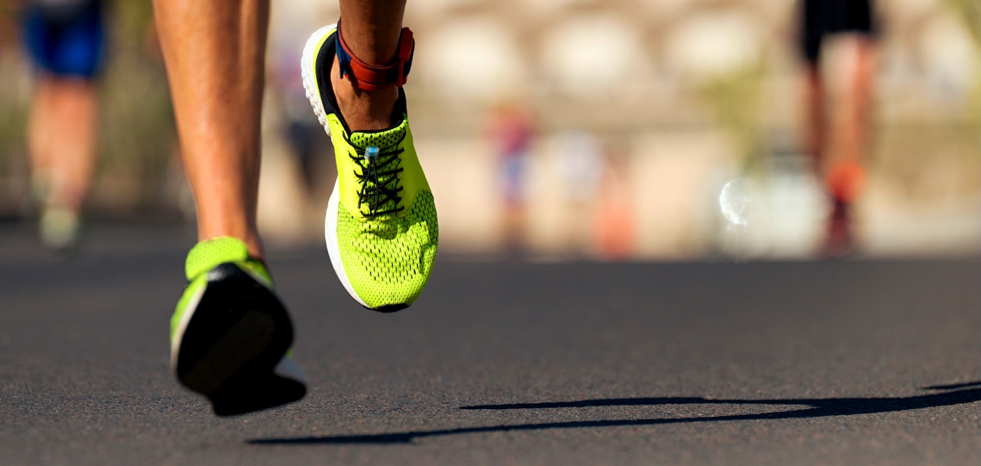 Close-up of a runner's neon green shoes in motion during a road race, with other runners in the background.