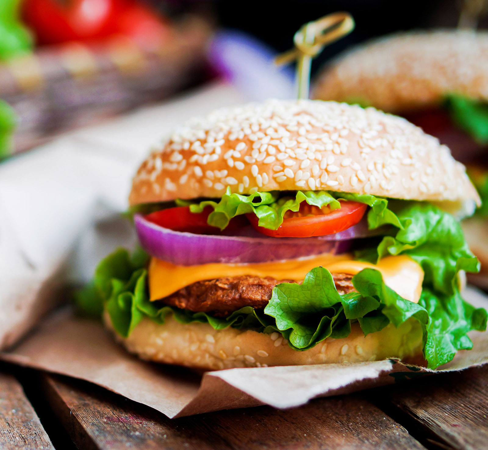 A close-up of a freshly made cheeseburger with lettuce, tomato, and onion on a sesame seed bun.