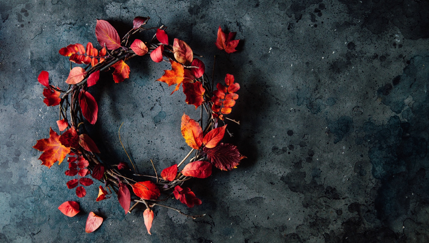 A wreath made of red and orange autumn leaves on a dark, textured background.