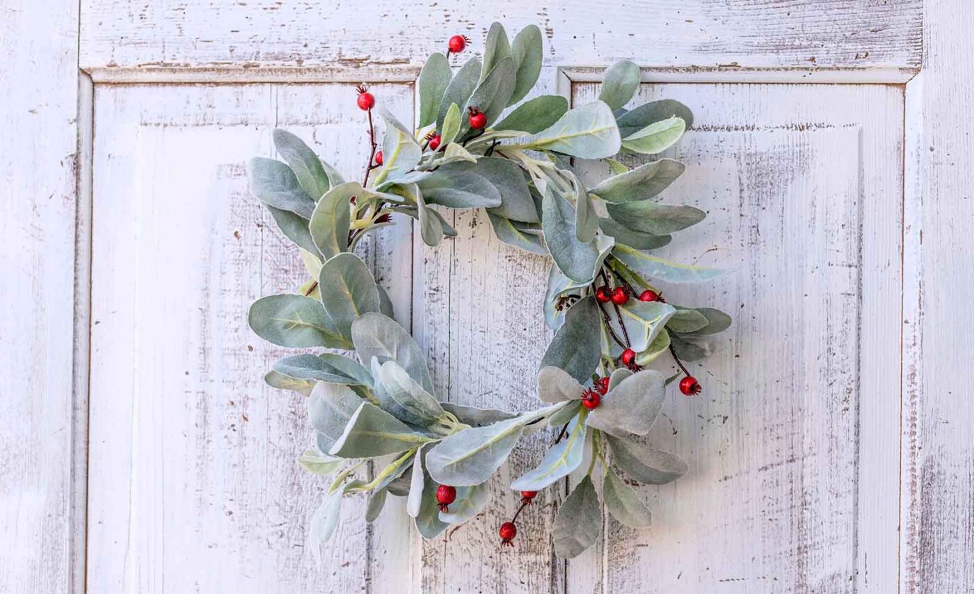 A wreath made of green leaves and red berries hanging on a white wooden door.