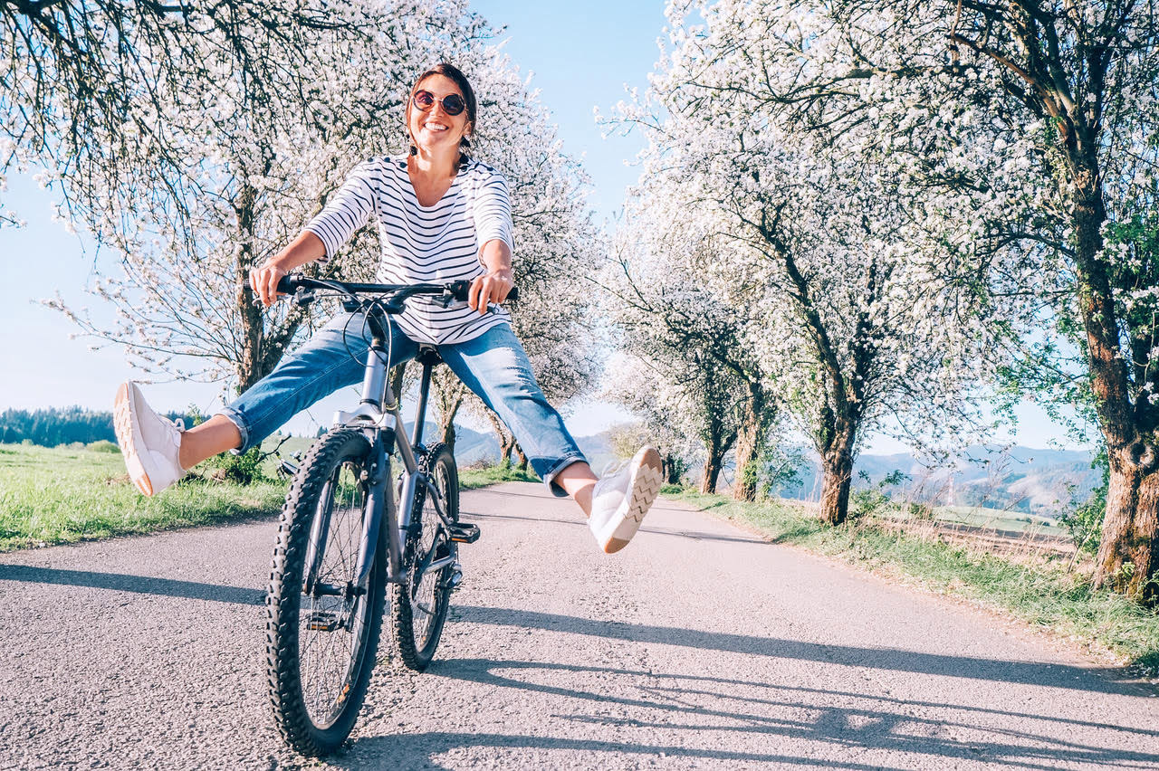 Woman riding bicycle with spring blossoms on trees in background