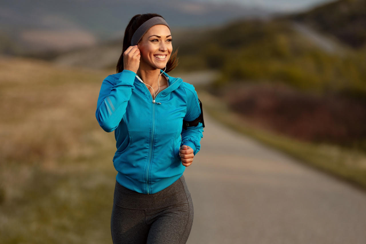 smiling woman running on a road adjusting ear bud