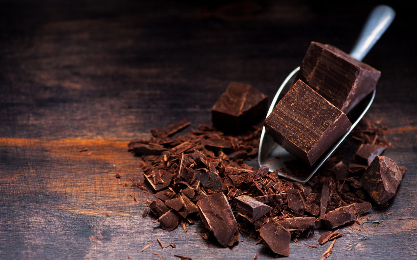 Chocolate chunks placed on a wooden table with silver scooper