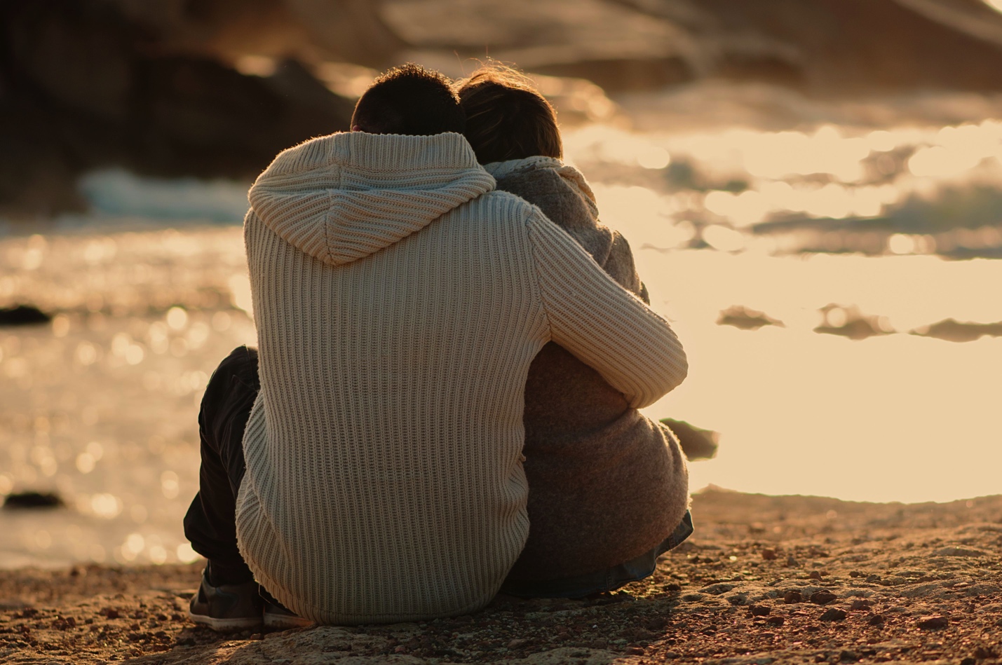 back of couple sitting, embracing at a waterfront